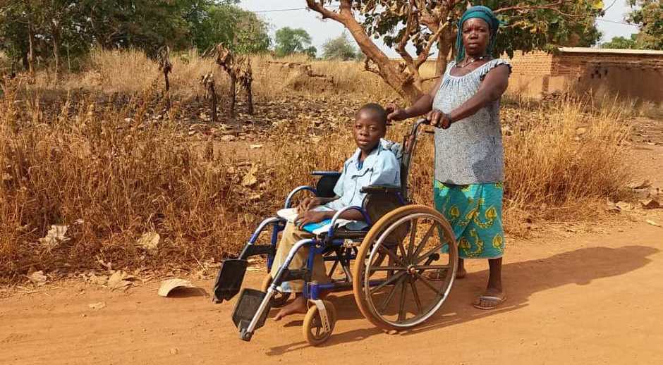 un enfant handicapé poussé dans son fauteuil roulant par une femme