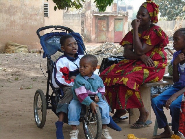 un enfant handicape dans son fauteuil roulant, un enfant assis devant lui et une femme
                                                                                             assise à côté 
